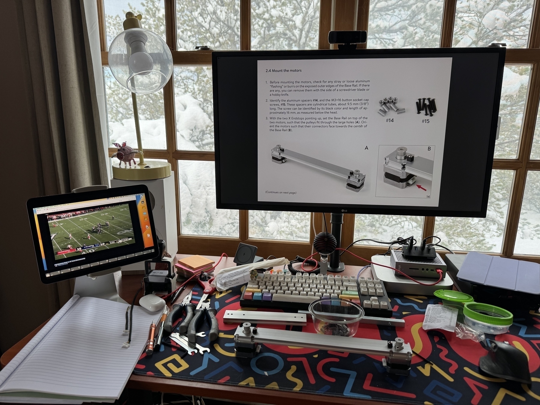 Ad hoc work surface at my desk with building in progress, Longhorns football on an iPad to the side, assembly instructions on computer screen, and snow covered trees out the window in the background.